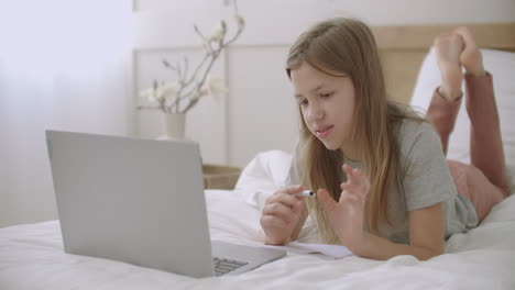 schoolgirl-is-communicating-with-teacher-by-video-call-on-laptop-lying-on-bed-in-home-online-lessons-for-secondary-schoolers-distant-education